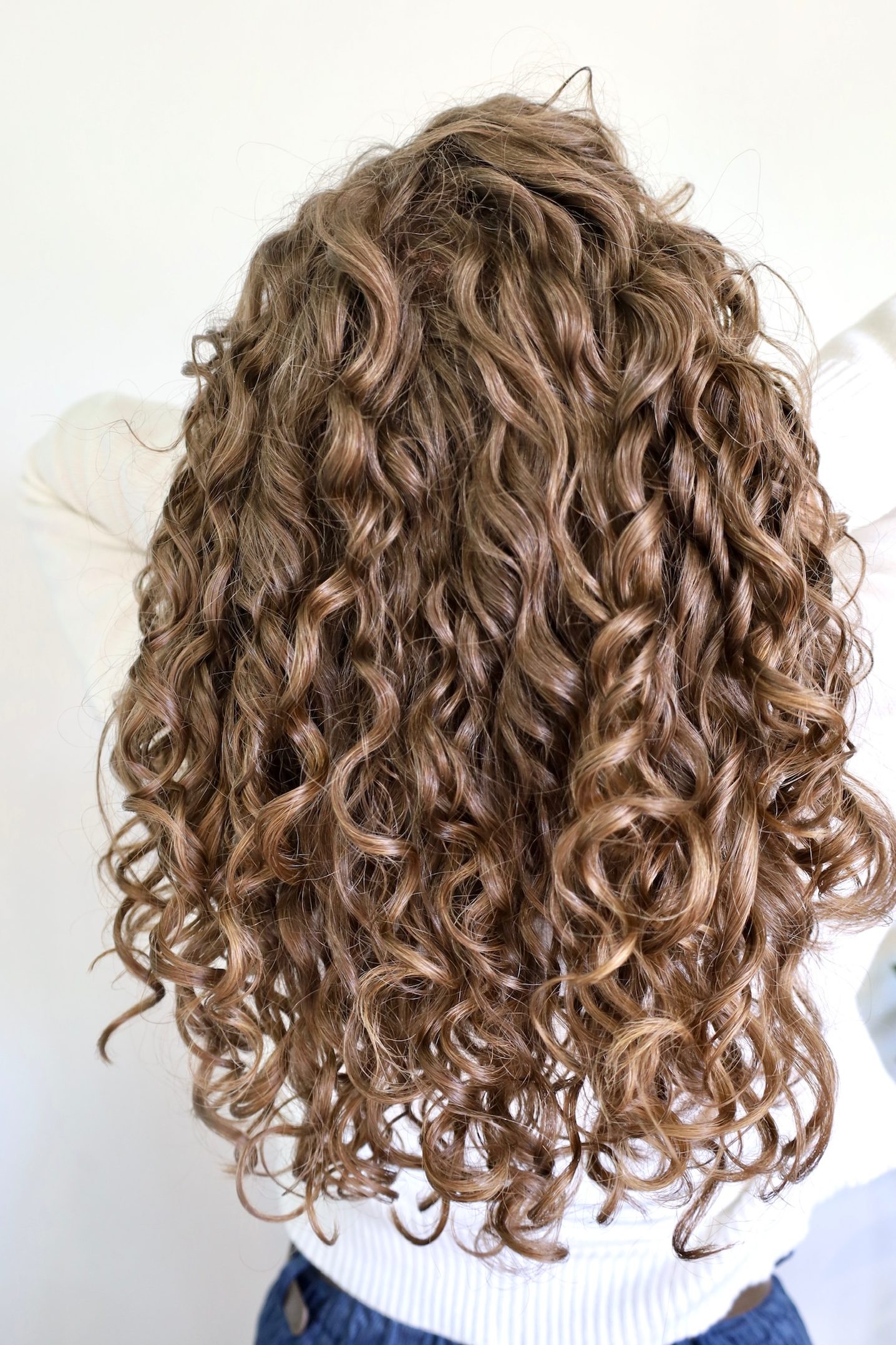 A photo of a woman with long, shiny, curly, brunette hair.